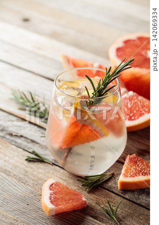 Gin tonic with ice, rosemary, and grapefruit slices on an old wooden table. Gin tonic with ice, rosemary, and grapefruit slices on an old wooden table. 142069334