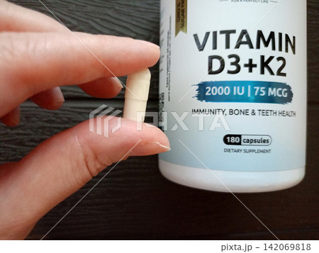 A vitamin D capsule between a woman's fingers A vitamin D capsule between a woman's fingers 142069818