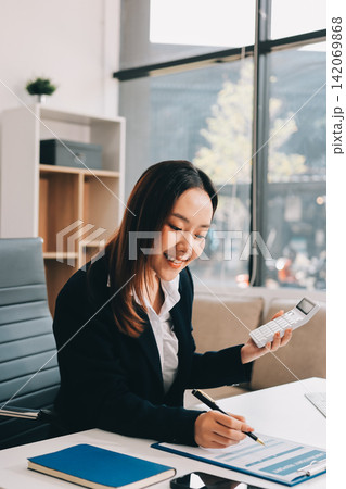 Asian businesswoman using calculator and working on laptop at modern office 142069868