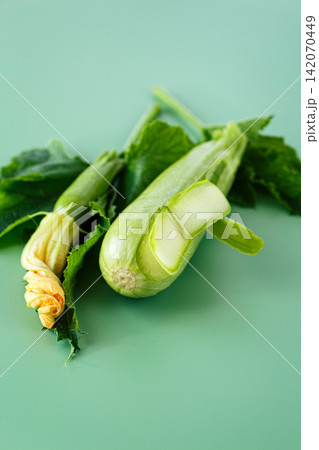Raw zucchini with peeled strips and yellow flower on green background 142070449