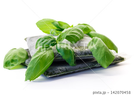 Fresh basil leaves arranged with frozen herb packages on white background Fresh basil leaves arranged with frozen herb packages on white background 142070458