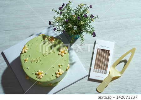 top view flat lay shot a green lime birthday cake with knight and a box of candles and small flower vase  on wooden table 142071237