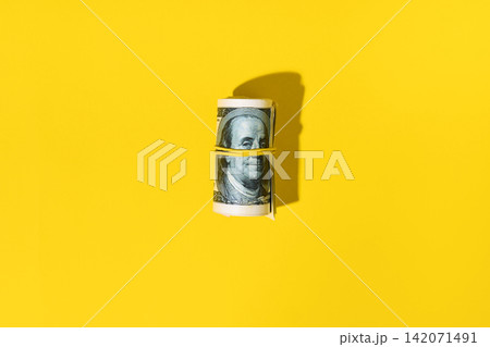 Roll of hundred dollar bills on yellow background Roll of hundred dollar bills on yellow background 142071491