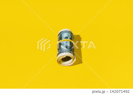 Roll of hundred dollar bills on yellow background Roll of hundred dollar bills on yellow background 142071492