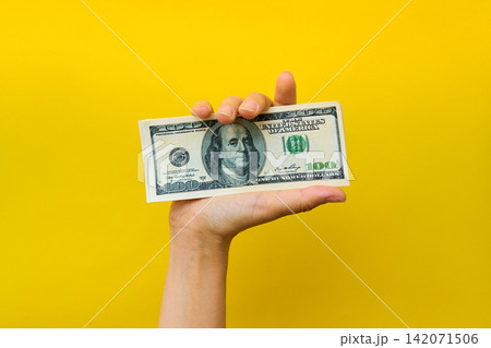 Hand holding hundred dollar bills on yellow background 142071506