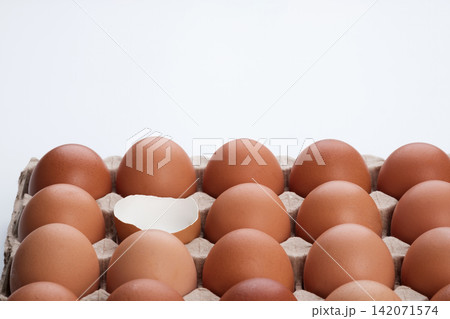 an opened empty cracked egg surround with full raw eggs in a tray on white background 142071574
