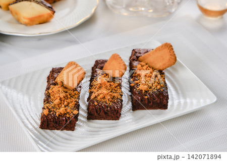 A decadent chocolate brownie sits on a white plate, accompanied by a steaming cup of English tea. The white tablecloth is spotless, adding to the elegant atmosphere. A decadent chocolate brownie sits on a white plate, accompanied by a steaming cup of English tea. The white tablecloth is spotless, adding to the elegant atmosphere. 142071894