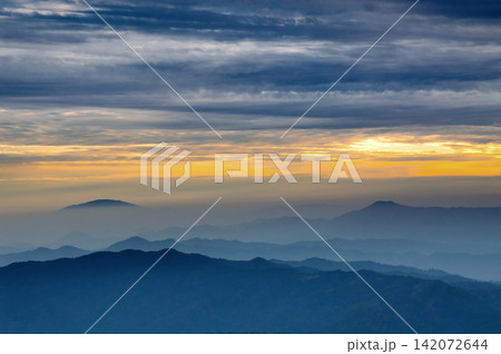sun rising over mountains with cloudy sky in rainy season and blue tone shadow and fogy scene below sun rising over mountains with cloudy sky in rainy season and blue tone shadow and fogy scene below 142072644