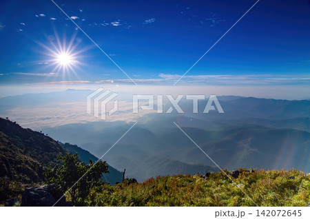 sunshine in colorful blue sky over village of hills scene from top of mountain high ground with some silhouette shade and wave of fog and mist below sunshine in colorful blue sky over village of hills scene from top of mountain high ground with some silhouette shade and wave of fog and mist below 142072645