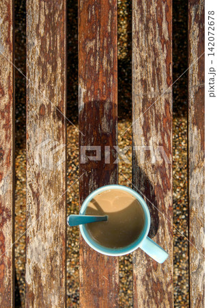 a cup of coffee on wooden bench in shade of morning sunrise with tea spoon looked like 7 o'clock's wall clock a cup of coffee on wooden bench in shade of morning sunrise with tea spoon looked like 7 o'clock's wall clock 142072678