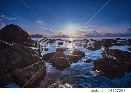 The sun rises over the horizon at the seaside, on a rocky beach. The waves wash over the rocks, creating a beautiful sight The sun rises over the horizon at the seaside, on a rocky beach. The waves wash over the rocks, creating a beautiful sight 142072684