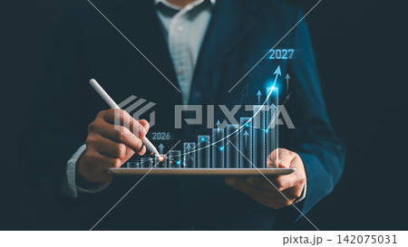 Businessman hand drawing glowing financial stock graph on tablet from year 2026 to 2027. Concept of business growth, investment return, future target forecast, planning strategy and success 142075031