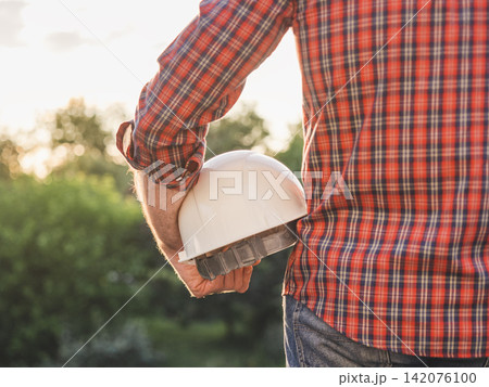 Construction worker holds a white hard hat Construction worker holds a white hard hat 142076100