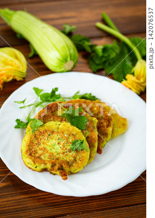 Golden fried zucchini pancakes with fresh herbs on wooden table background Golden fried zucchini pancakes with fresh herbs on wooden table background 142076537