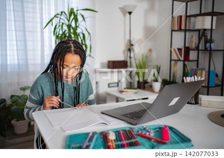 Girl completing homework at desk with laptop for remote learning 142077033