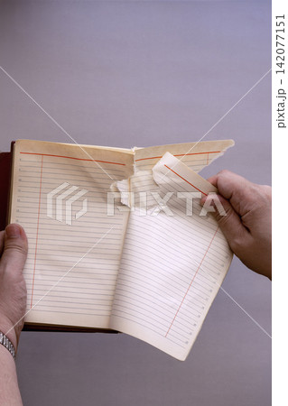 Hands tearing a blank page out of an open lined notebook on a grey background. 142077151