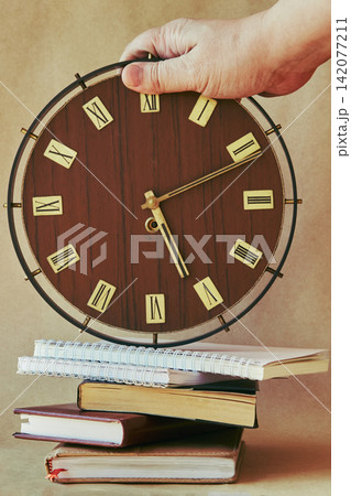 Large old clocks with Roman numerals stand on notebooks and organizers. Large old clocks with Roman numerals stand on notebooks and organizers. 142077211