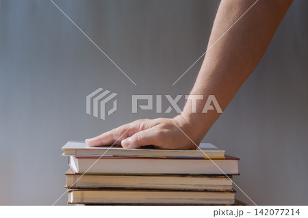 Hand Resting on Stack of Books Symbolizing Study, Learning, Education and Knowledge 142077214