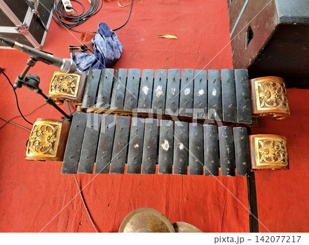 Metal keyed xylophone instrument known as saron used in Indonesian gamelan orchestra set against bright red stage carpet flooring. 142077217
