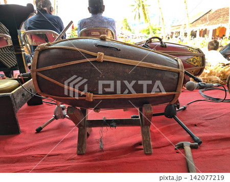 Hand crafted cylindrical drum instrument made of wood and leather straps placed on wooden stand for gamelan ensemble performances. Hand crafted cylindrical drum instrument made of wood and leather straps placed on wooden stand for gamelan ensemble performances. 142077219