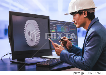 Engineer in a hard hat reviewing a gear design on a computer screen while using a tablet and stylus in a modern office. Engineer in a hard hat reviewing a gear design on a computer screen while using a tablet and stylus in a modern office. 142077615