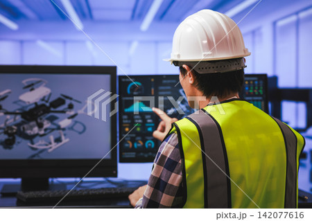 Engineer in hard hat and safety vest working at computer screens with a drone model and data display in a modern lab 142077616