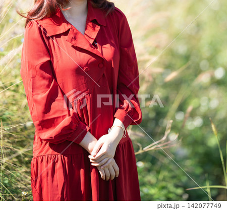 woman wearing a red dress walking through a tall grass field. woman wearing a red dress walking through a tall grass field. 142077749