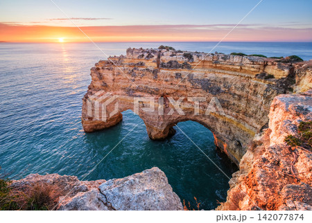Sunrise at Praia da Marinha beach in Algarve, Portugal, with ocean cliffs, sea stacks and bright clouds over the sea. Sunrise at Praia da Marinha beach in Algarve, Portugal, with ocean cliffs, sea stacks and bright clouds over the sea. 142077874