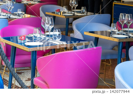 Elegant Restaurant Interior with Modern Pink and Blue Chairs, Glassware, and Set Tables for Fine Dining Elegant Restaurant Interior with Modern Pink and Blue Chairs, Glassware, and Set Tables for Fine Dining 142077944
