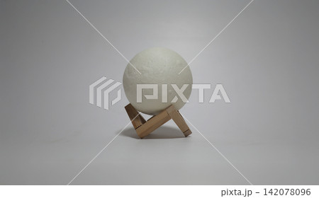 White spherical lamp resting on a small wooden tripod stand against a plain background, creating a minimalist interior object composition with modern design and soft neutral tones 142078096