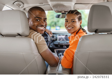Smiling young Black couple turning toward camera from front seats of car Smiling young Black couple turning toward camera from front seats of car 142078331