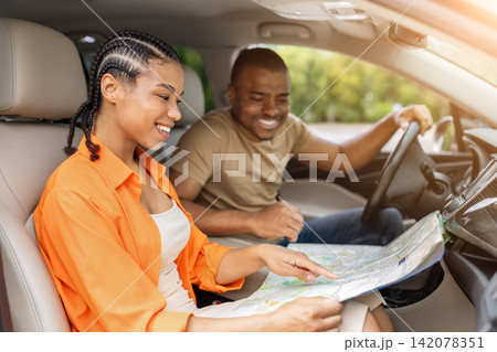 Young Black couple smiling inside car while studying a paper map together 142078351