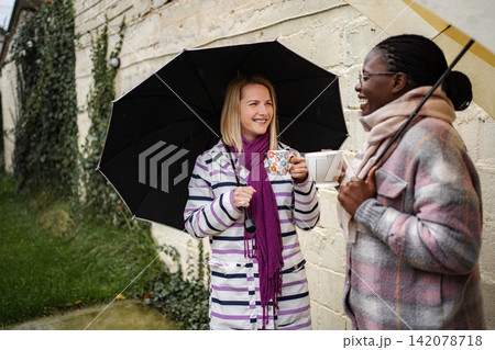 Two women enjoying coffee together under umbrellas during rain Two women enjoying coffee together under umbrellas during rain 142078718