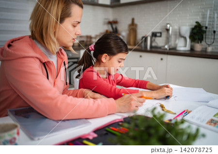 Mother helping young daughter with homework at home kitchen 142078725