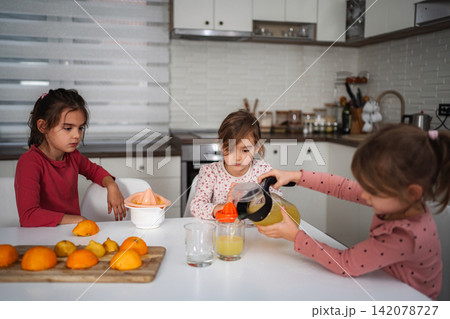 Girls pouring fresh orange juice for breakfast in kitchen 142078727
