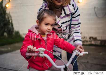 Mother helping child learn riding bicycle outdoors Mother helping child learn riding bicycle outdoors 142078764