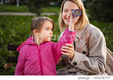 Mother and daughter playing with toy telescope in park Mother and daughter playing with toy telescope in park 142078777