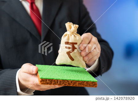 A plot of land and a Indian rupee money bag. Land purchase. Valuation. Leasing a plot of land for construction. Purchase for construction and projects. A plot of land and a Indian rupee money bag. Land purchase. Valuation. Leasing a plot of land for construction. Purchase for construction and projects. 142078920