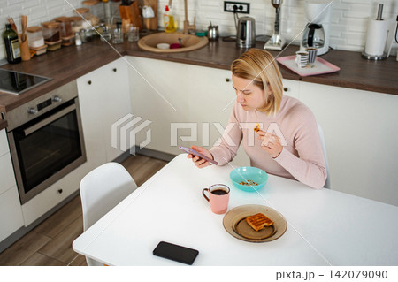 Woman using smartphone while eating breakfast and drinking coffee 142079090
