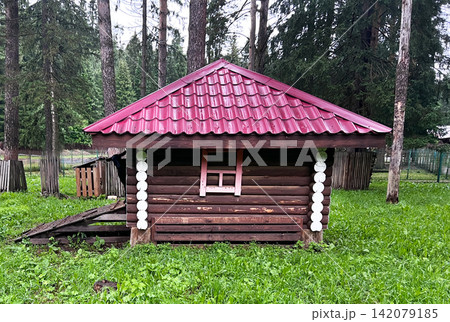 goat looks out small wooden log cabin with red metal roof in pine forest. Rustic shed surrounded by green grass. Traditional timber architecture for garden storage or rural countryside landscape. goat looks out small wooden log cabin with red metal roof in pine forest. Rustic shed surrounded by green grass. Traditional timber architecture for garden storage or rural countryside landscape. 142079185