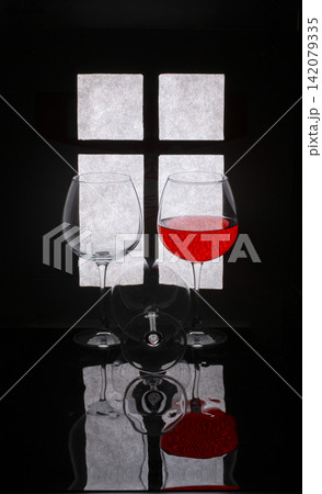 Still life with glasses and red wine against the background of a window silhouette 142079335