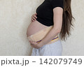 Close-up maternity photo of a pregnant woman wearing a supportive belly band and gently holding her baby bump. Concept of pregnancy care, comfort, health, and expecting motherhood. 142079749