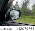 Rainy road trip view through car side mirror with water drops 142079763