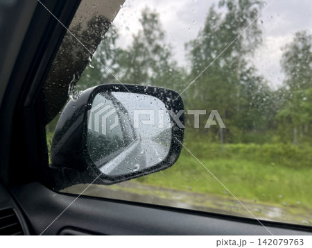 Rainy road trip view through car side mirror with water drops Rainy road trip view through car side mirror with water drops 142079763