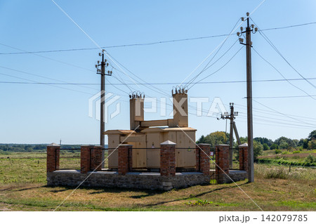 Electrical transformer substation with power poles in rural field under blue sky Electrical transformer substation with power poles in rural field under blue sky 142079785