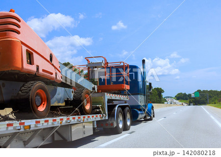 Transportation truck carries construction machinery on trailer along highway 142080218