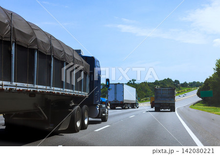 Several large trucks travel on US interstate highway in American rural area. 142080221