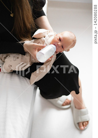 A caring mother gently feeds her newborn baby with a bottle while holding the infant close in her arms A caring mother gently feeds her newborn baby with a bottle while holding the infant close in her arms 142080288