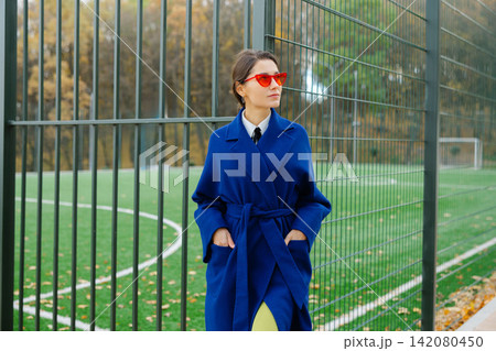 Beautiful woman relaxing at the park near sportground wearing autumn clothing. Young smiling woman confident looking at camera Beautiful woman relaxing at the park near sportground wearing autumn clothing. Young smiling woman confident looking at camera 142080450
