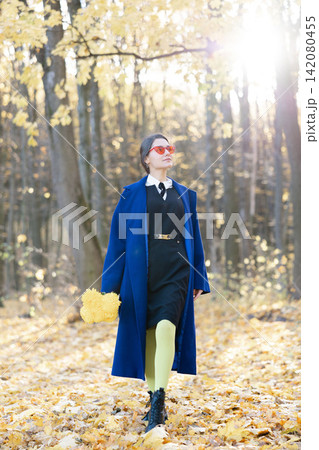 Young woman in sunglasses walking in forest, wearing blue coat with boquet. Autumn trendy fashion 142080455